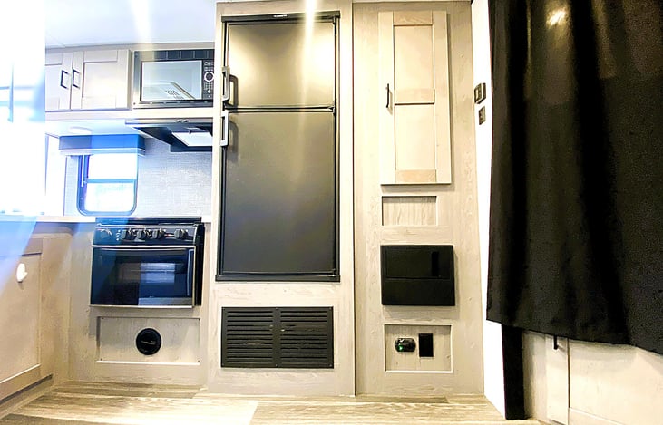 Hallway shot with fridge, pantry, and central control panel — perfect layout for weekend adventures to Glamis, San Luis Obispo, or Malibu. Great for those seeking RV rent near me.