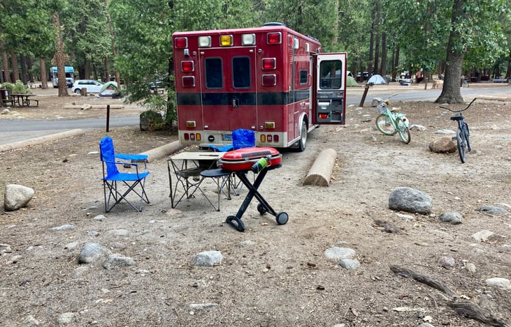 Campsite set up with two foldable camping chairs, folding table, and Coleman portable propane grill