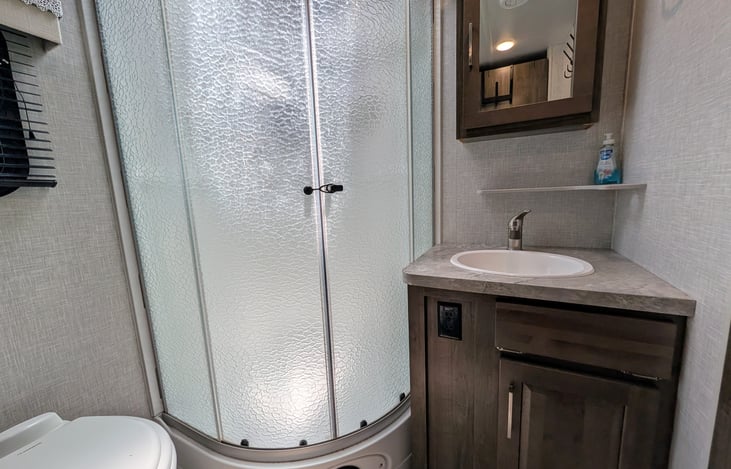 Spacious bathroom with large corner shower, glass door, and skylight for extra headroom! Includes a porcelain foot-flush toilet, medicine cabinet, vanity, and plenty of towel storage + washer/dryer.