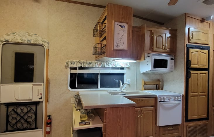 Kitchen with 3 burner stove, refrigerator/freezer, and microwave.   Toaster and icemaker on shelf below counter.  Entry door on left.