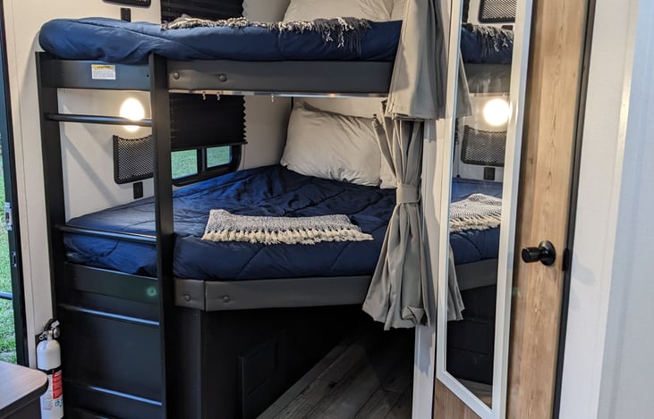 Double-over bunk beds with privacy curtains, dual USB charging ports, and phone storage. The bottom bunk folds up and locks to provide additional storage.