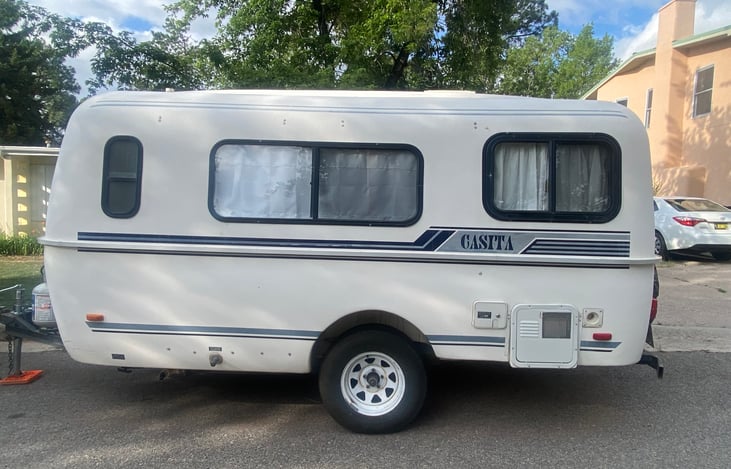Casita driver side view with door to electrical hook up shown, as well as city water connection, and black and gray water drains.