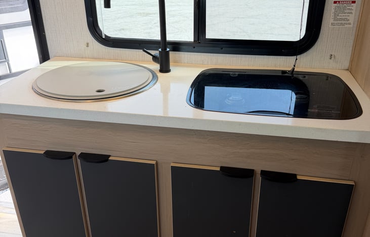 Cook with ease! Features a high-efficiency refrigerator, dual-burner cooktop, deep sink, and fully stocked utensils, pots, and pans for seamless campsite meals.