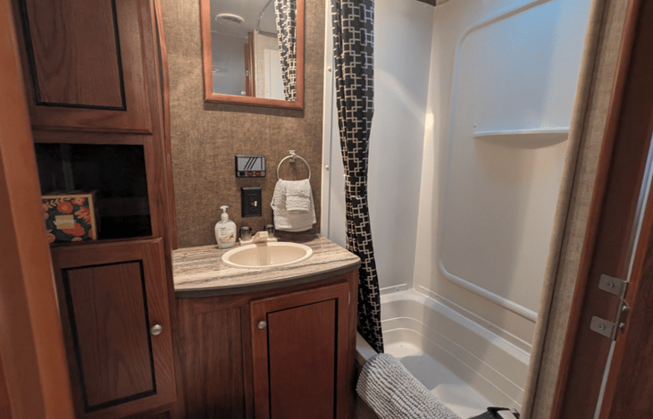Bathroom is equipped with a shower/tub combo, storage cabinets and toilet.
