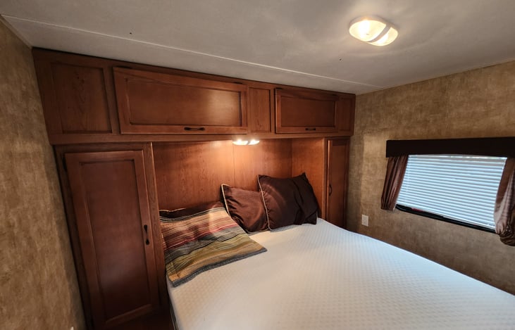 Back bedroom with queen bed, closet cabinets on both sides, and storage above bed. A door separates bedroom from hallway (to right out of view).