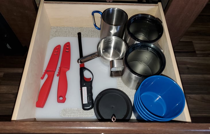 2nd drawer in kitchen: coffee cups, measuring cup, lighter, cutting board, knives, and small cups with sip lids.