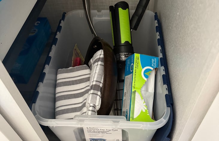 under the sink storage- includes some camp essential: small frying pan, cleaning supplies, rechargeable camp light