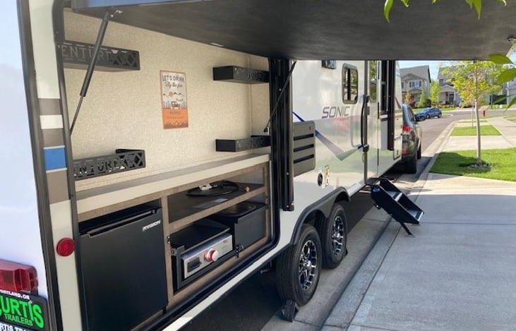 Outdoor kitchen with fridge, stove, and sink.