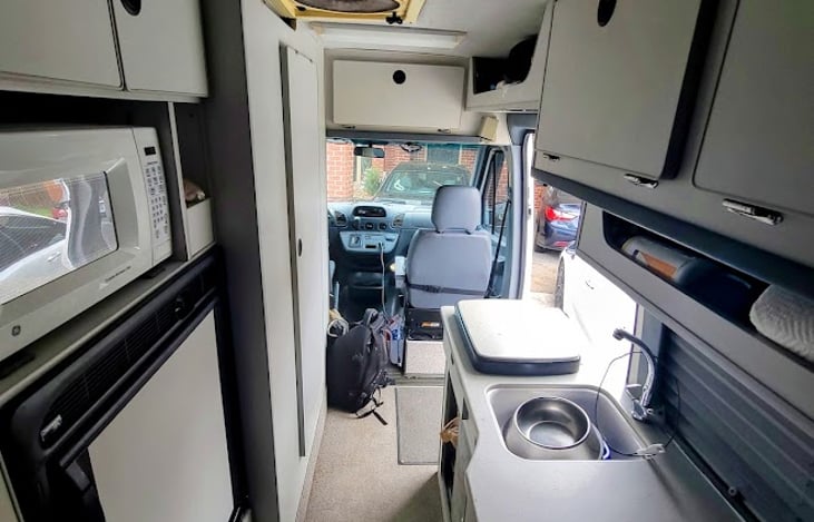 Sink, fridge, microwave, stove, tons of cabinet storage, and bathroom with shower on left.