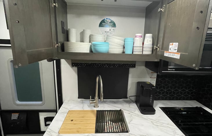 Stocked with plates, bowls, cups, coffee cups, and Keurig machine.