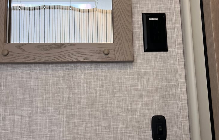 The side wall in the bathroom has its own light switch, an outlet for the hair dryer, and a mirror.