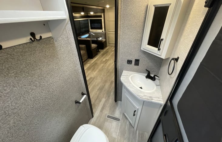 Inside bathroom with sink, toilet, and stand up shower, storage and back door hanger.