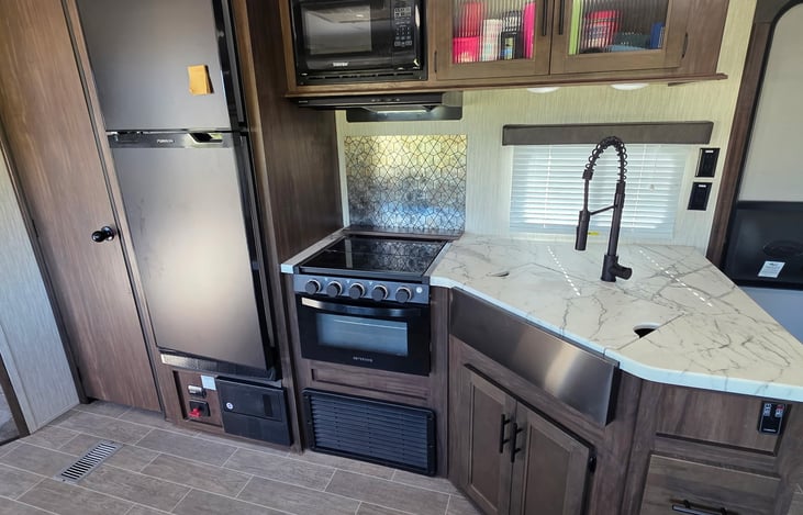 Full functional kitchen with large fridge, stove/oven, microwave, exhaust fan, and handheld sprayer over the farmhouse sink.