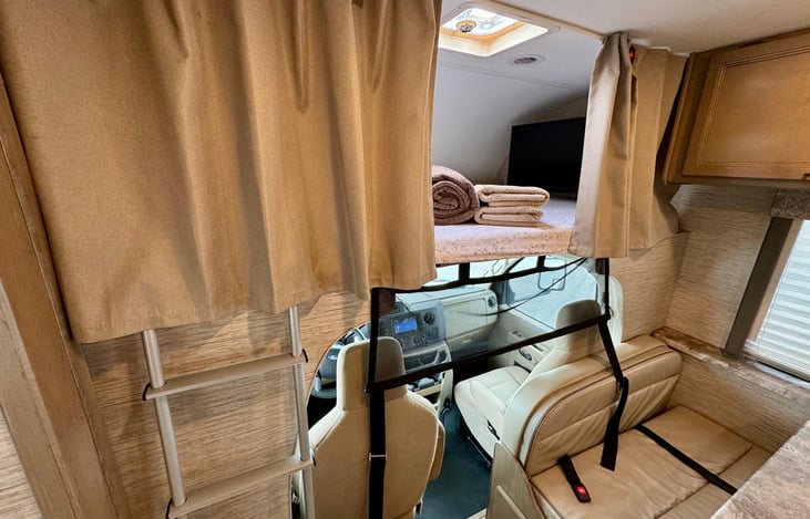 Spacious queen bunk bed above the driver's cabin, accessible by ladder. Offers a cozy, elevated sleeping space with privacy—ideal for adults or kids who love unique sleeping spots!