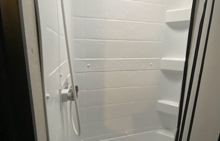 Shower in bathroom with overhead window and side shelves.