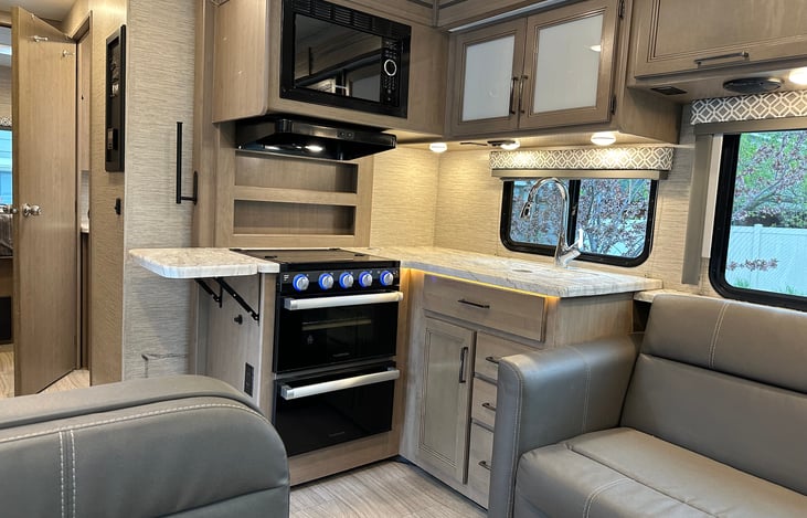 Small oven and a 3 burner gas stove, microwave and food prep area tray. The sink also has a cover adding to the counter space.