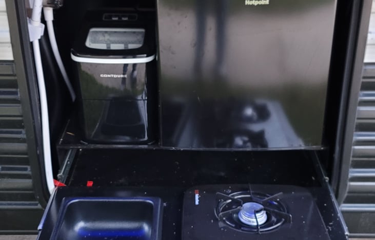 Outdoor kitchen area with drink refrigerator, dual burner stove, ice maker, and cold/hot water source.