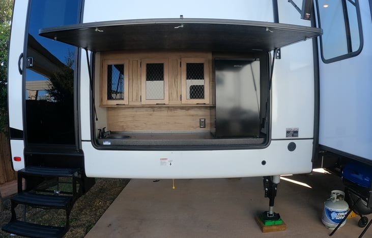 Outdoor kitchen includes cabinet storage, sink and refrigerator