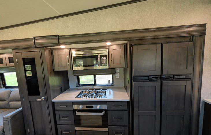 Gourmet galley & rear den retreat! Includes a 12 cu ft fridge, pantry, stove/oven, dual sofas, theater seats, 50" TV, electric fireplace, and 3 slides for spacious high-end living.