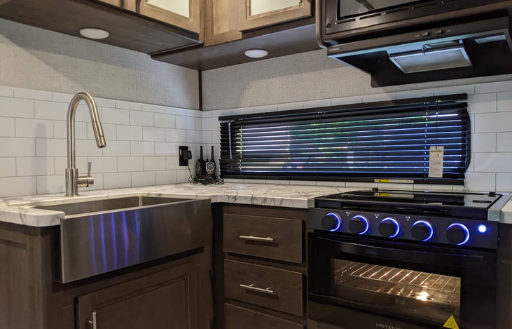 A farm-style sink. 3 burner gas stove with oven, microwave.  Basic ingredients: BBQ rubs, salt & pepper, oil, disposables, & cleaning items.