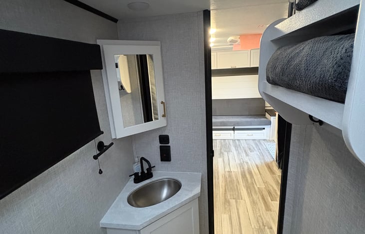 Bathroom sink, vanity, storage, hooks as well as body and hand towels.