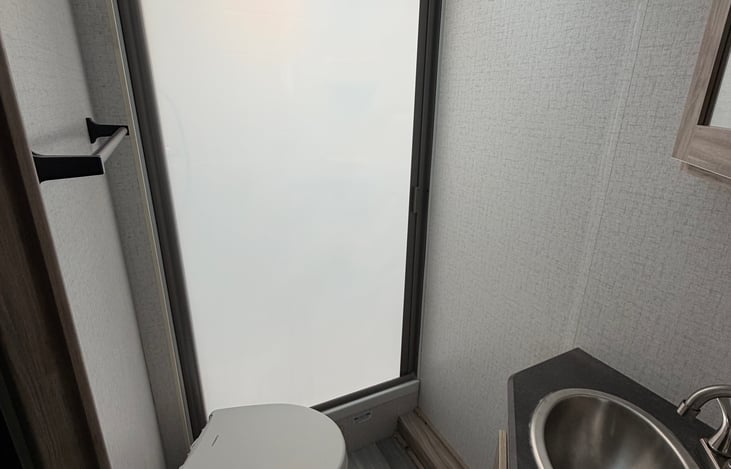 Restroom, features retractable frosted shower door for privacy as well as toilet and sink with GFCI outlet and storage (both over and under the sink)