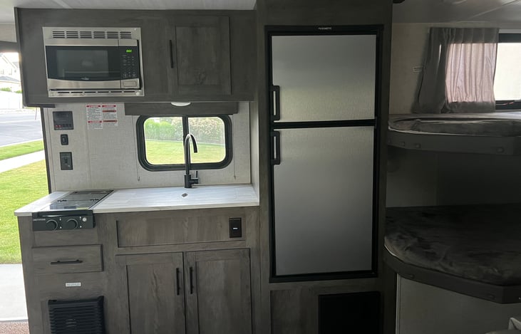 Kitchen with microwave, 2 burner gas stove top, refrigerator/freezer, upper and lower cabinets, and large sink.