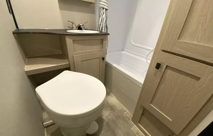 Bathroom toilet with foot flush (angled to provide ample elbow room), wardrobe storage cabinet and sink with storage cabinet and shelf