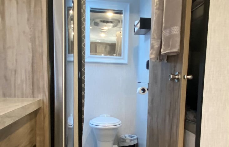 Bathroom area has a porcelain toilet, mirror, and shelf for toiletries items.