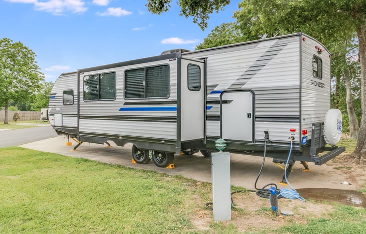 Left side of travel trailer. Showing slideout, back door, water hookup, electric hookup and sewer hookup.