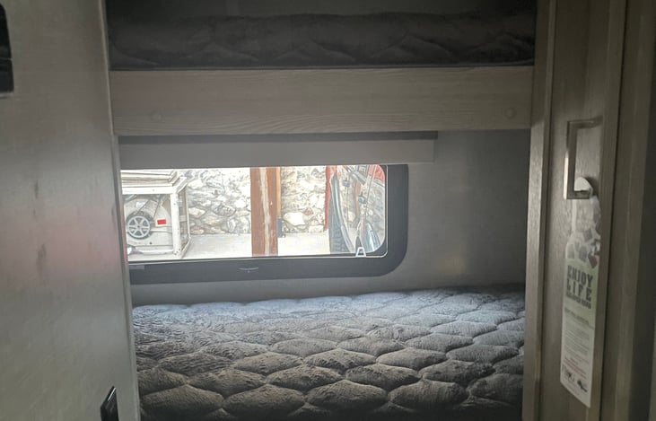 Bunk bed mattresses, window with pull down panel and small closet.