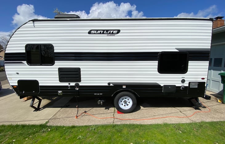 Left side of RV: front storage, power hookup, grey and black tank outlets, shower, water outlets