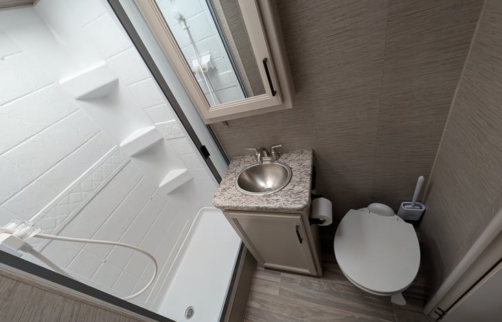 Private rear bathroom features a spacious corner shower with a skylight for extra headroom, a foot-flush toilet, a vanity sink with storage, and a large mirror. Perfectly clean and functional!