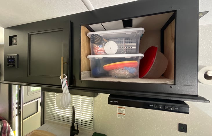 Behind door is some cooking seasonings and other items. In containers is coffee with a percolator and filters. Also cooking tools, plates and bowls. Coffee mugs are behind door.