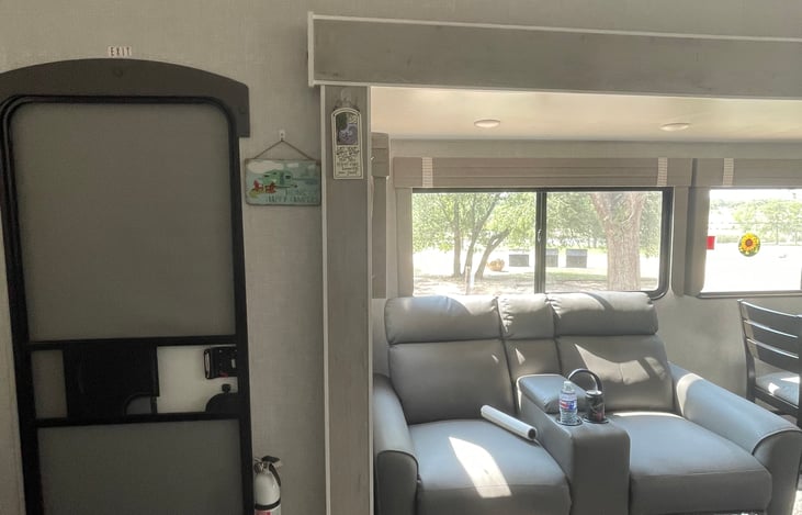 This RV is surrounded by windows with views from every direction. Here shown is the door leading into the living area. Plus, the two recliners that sit opposite of the T and fireplace.