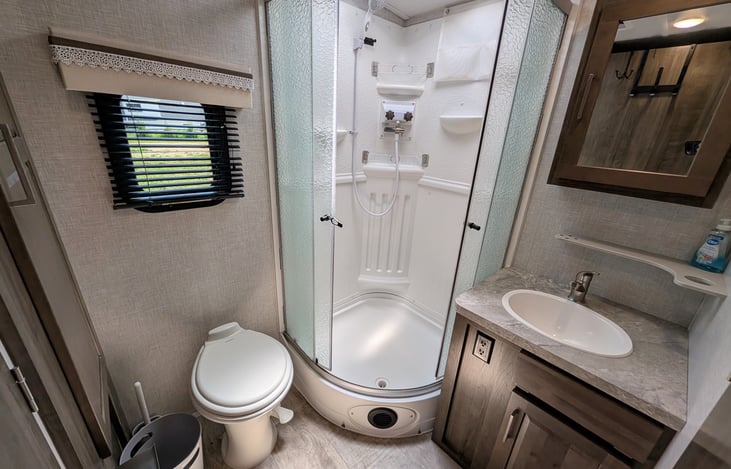 Spacious bathroom with large corner shower, glass door, and skylight for extra headroom! Includes a porcelain foot-flush toilet, medicine cabinet, vanity, and plenty of towel storage + washer/dryer.