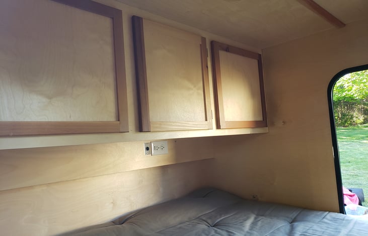 Cabinetry, foot of the queen mattress,  and interior outlets. 12v interior outlet is live from the camper's battery. 110v outlet is live when the camper is attached to shore power.