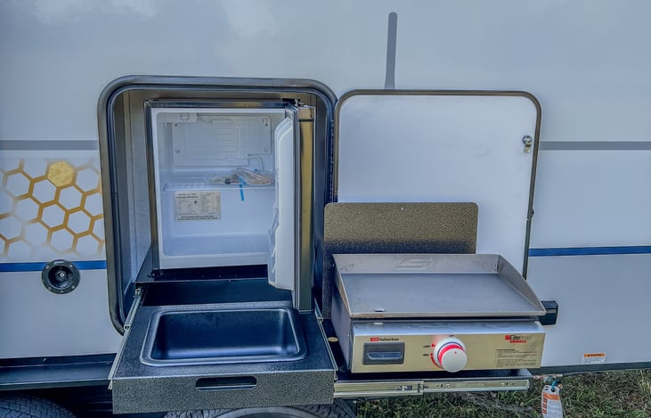 Outdoor kitchen with griddle, sink, and fridge.