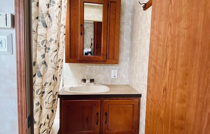 Bathroom area with full tub. Towels are located under the sink and bathroom items in the medicine cabinet.