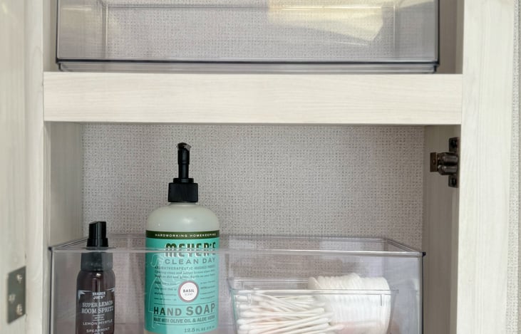 Bathroom cupboard includes bins for bathroom essentials. Hand soap and a few other basics are included.