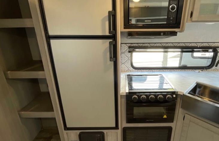 The Kitchen! ……..Oven and Stove with Refrigerator and small freezer and our kitchen sink. Underneath is our cleaning supplies and collapsible drain board and bucket.