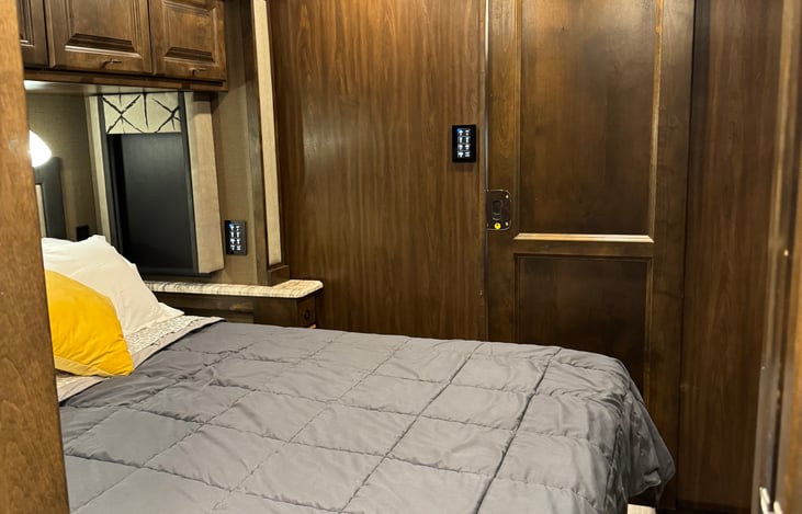 bedroom with view of privacy door, overhead storage. Large closet with mirror & additional storage are located across from the bed.