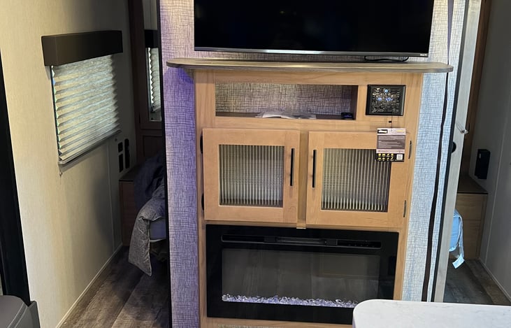 Tv and fire place, entertainment system control panel in middle, connect Bluetooth capable with speakers throughout the trailer and outside