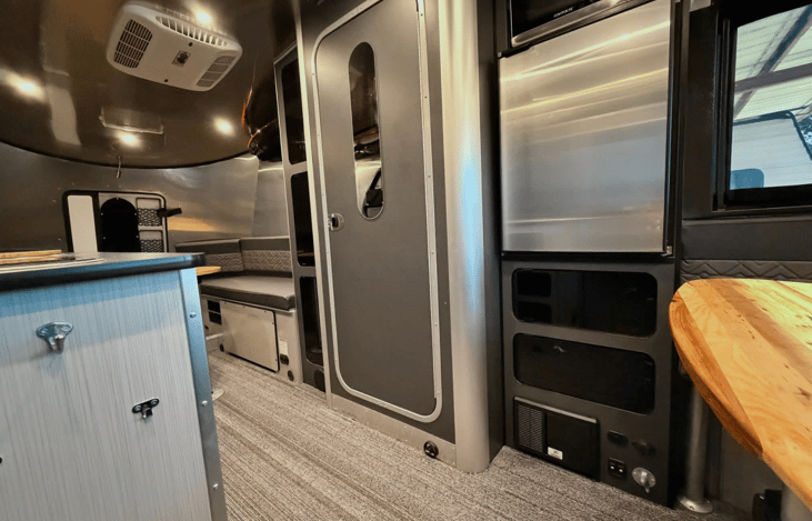 The entry view highlights the Basecamp 20X’s exceptional space efficiency and premium amenities. The central door opens to a full onboard wet bath, providing a private shower and toilet.