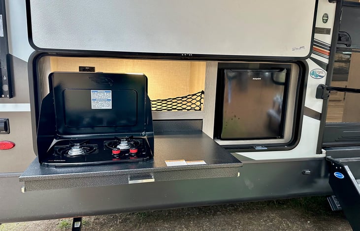 Outdoor kitchen with small drink fridge and 2 burners. plus storage area above with flat grill.
