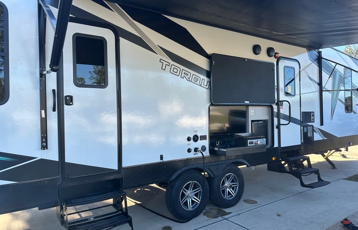Outside has a mini fridge, small griddle, and a sink. TV located above the appliances.