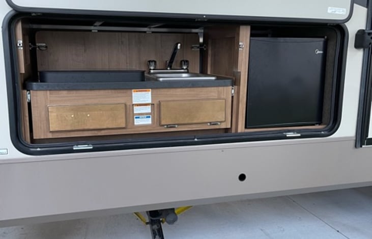 Outside kitchen area with two burner range, sink with hot & cold running water and small fridge with freezer compartment.