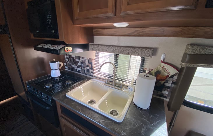 Kitchen area with working stove, microwave, oven and refrigerator. Kitchen is stocked with all essentials such as pots and pans, cooking utensils, paper plates, plastic silverware, cups, etc.