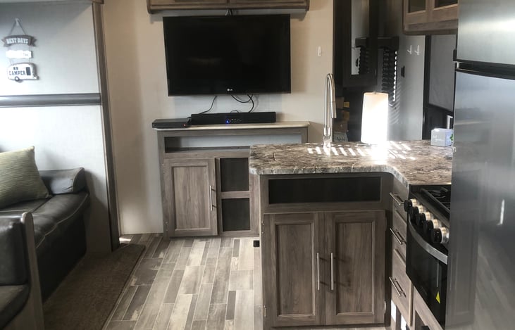 Couch to the left, TV, DVD, AM/FM Bluetooth Soundbar, kitchen to the right