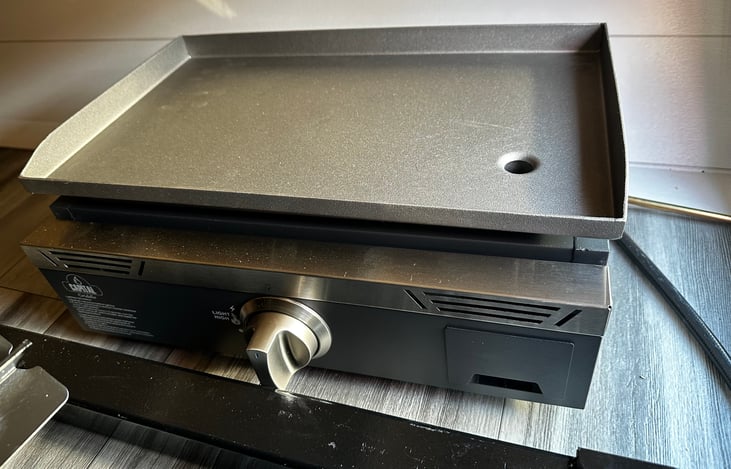 Outdoor griddle is stored in front compartment, attaches to back of camper on the door side